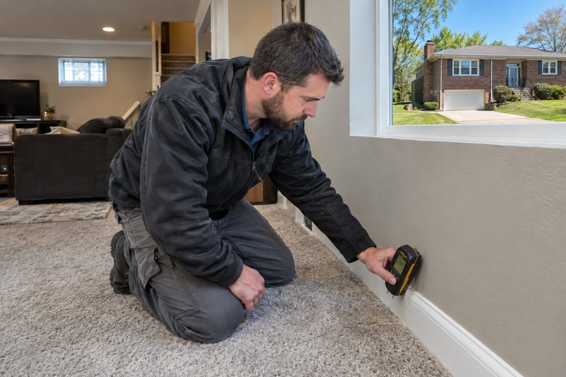 A close view of a technician checking moisture along finished-basement baseboards in a Riverside Northland home in Riverside, MO